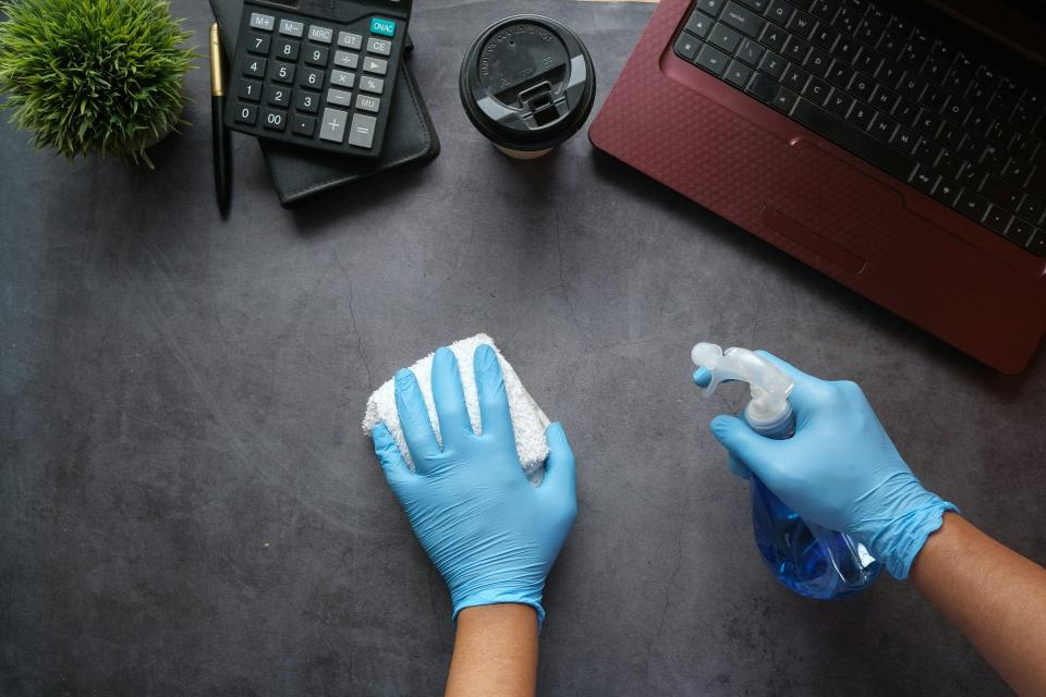 Gloves wiping office desk using cleaning supplies